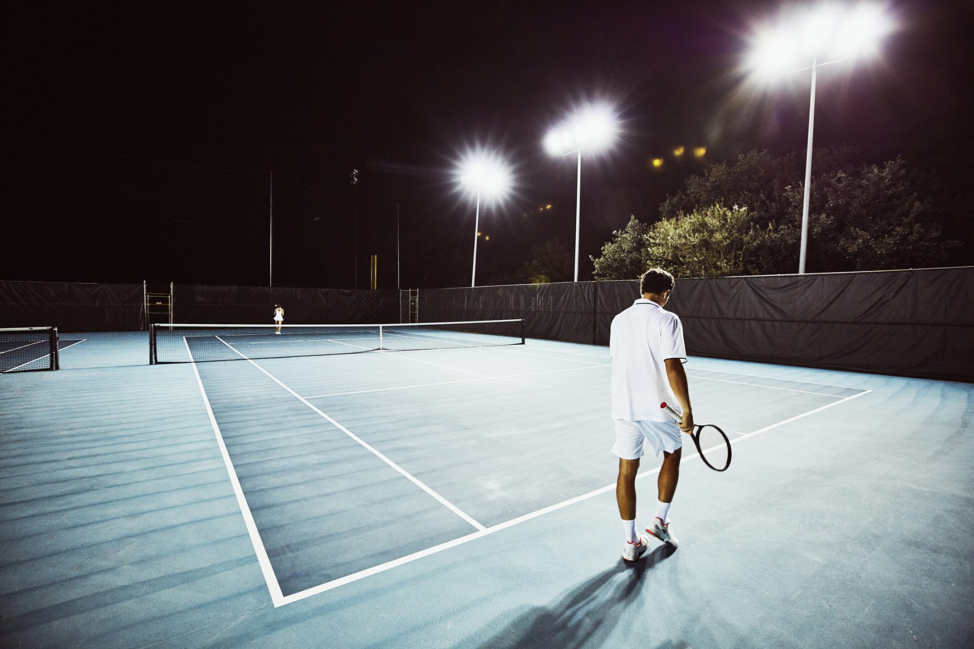 Tennis teammates practicing together on outdoor court at night