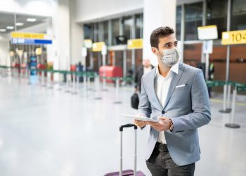 Businessman holding digital tablet at airport using protective mask