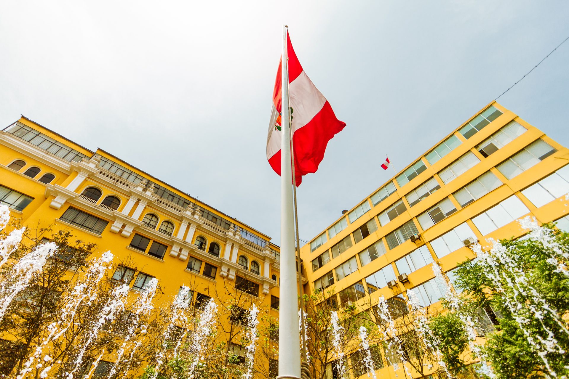 Peruvian flag waving next to a fountain and in front of two buildings in Lima, Peru