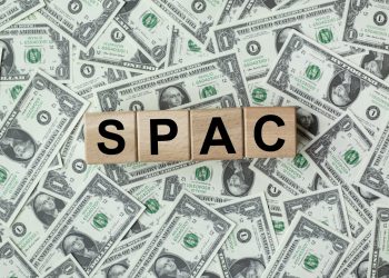 SPAC, special purpose acquisition company symbol. Wooden cubes with word 'SPAC' on beautiful background from dollar bills, copy space. Business and SPAC, special purpose acquisition company concept.