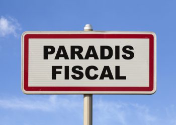 A French entry city sign against a blue sky with written in the middle in French "Paradis fiscal", meaning in English "Tax haven".