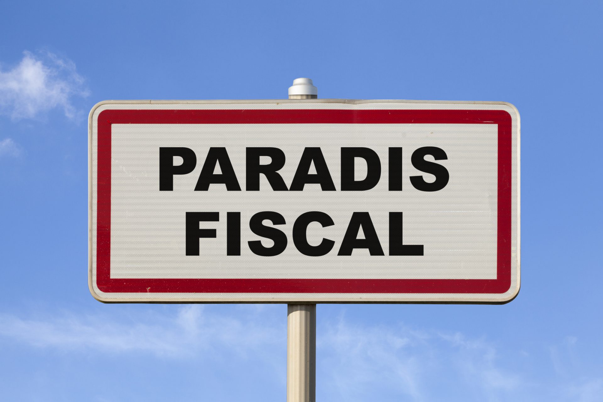 A French entry city sign against a blue sky with written in the middle in French "Paradis fiscal", meaning in English "Tax haven".