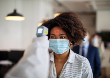 Woman wearing protective mask goes through a temperature checks before going to work in the office. New SOP in office to prevent illness.
