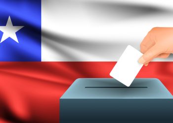 Male hand puts down a white sheet of paper with a mark as a symbol of a ballot paper against the background of the Chile flag. Chile the symbol of elections