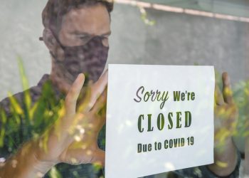 Portrait shot of business manputting a closing announcement message into the restaurant window due to Covid 19 pandemic