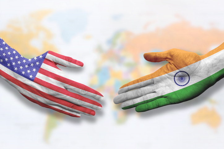 Hands colored like the flags of India and the United States symbolizing cooperation and friendship. Offering a handshake.