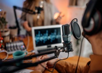 Selective focus of microphone used by young man and woman while recording podcast during interview and doing live broadcast in studio
