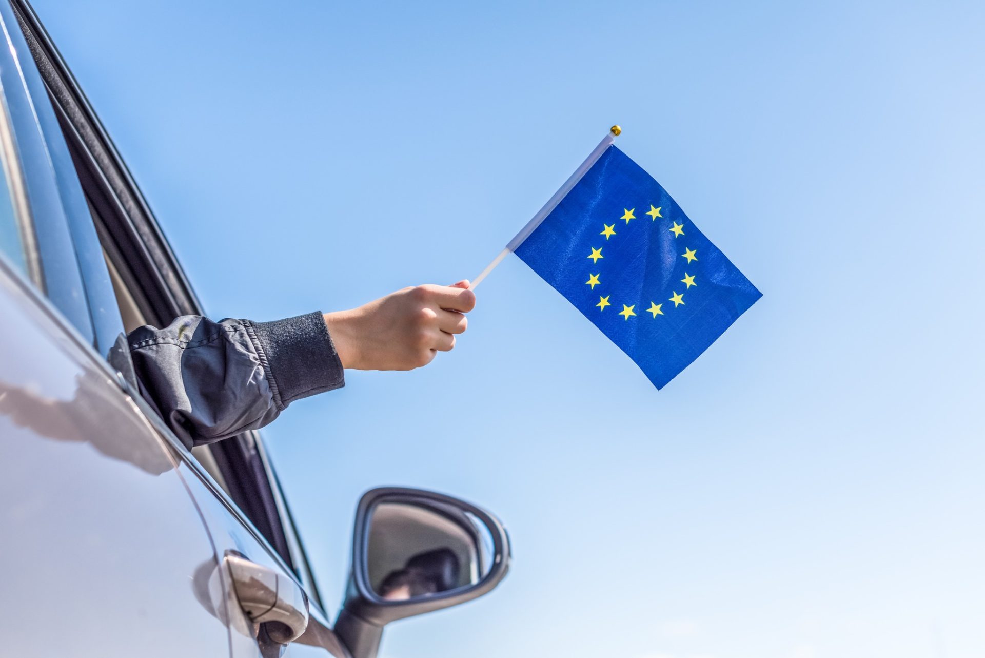 Boy holding Europe or European(EU) Flag from the open car window on the sky background. Concept.