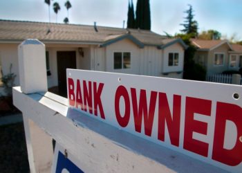 A foreclosed home shows a bank owned for sale sign.