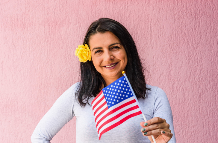 Woman holds flag of United States in front of isolated wall background