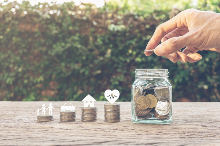 Savings money for family life concepts. Hand holding coin on a full money in glass jar and family member, car, house, healthy on coins. Depicts saving for wealth and life. fundraising concept.
