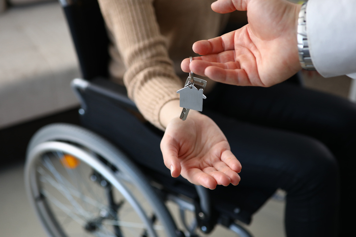 Close-up of Real Estate Agent putting keys from new apartment on owners hand. Person sitting in wheelchair. Disabled people. Buy property. Real estate and mortgage concept