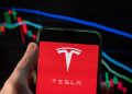 CHINA - 2021/12/09: In this photo illustration the American EV electric car manufacturing company brand Tesla logo seen displayed on a smartphone with an economic stock exchange index graph in the background. (Photo Illustration by Budrul Chukrut/SOPA Images/LightRocket via Getty Images)