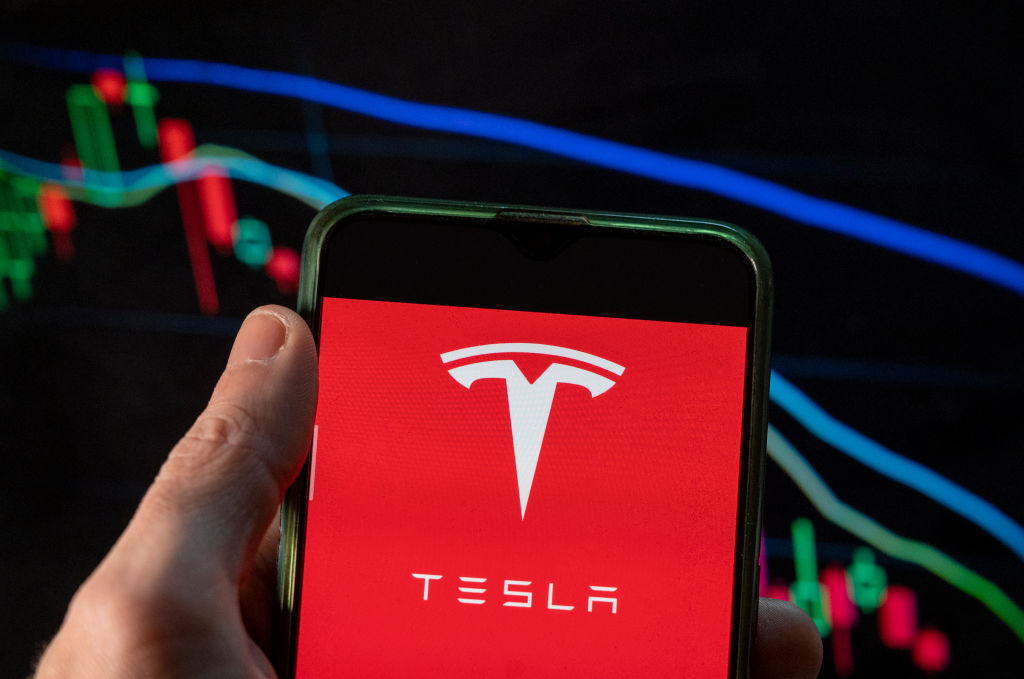CHINA - 2021/12/09: In this photo illustration the American EV electric car manufacturing company brand Tesla logo seen displayed on a smartphone with an economic stock exchange index graph in the background. (Photo Illustration by Budrul Chukrut/SOPA Images/LightRocket via Getty Images)