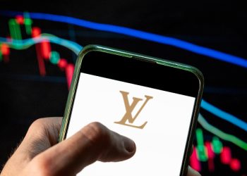 CHINA - 2021/12/09: In this photo illustration the French luxury fashion brand Louis Vuitton (LV) logo seen displayed on a smartphone with an economic stock exchange index graph in the background. (Photo Illustration by Budrul Chukrut/SOPA Images/LightRocket via Getty Images)