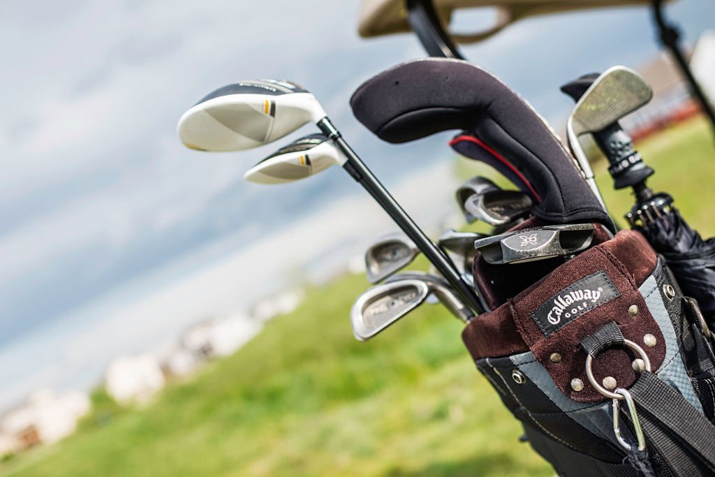 Peyton, Colorado, USA - June 13, 2015: A horizontal format shot of a Callaway golf bag filled with assorted golf clubs on the back of a golf cart. In the golf bag are Ping Eye 2 irons, an Odyssey putter, a Callaway Big Bertha Steelhead Plus driver and Taylormade Rocketballz (RBZ) clubs. In the background is a defocused green.