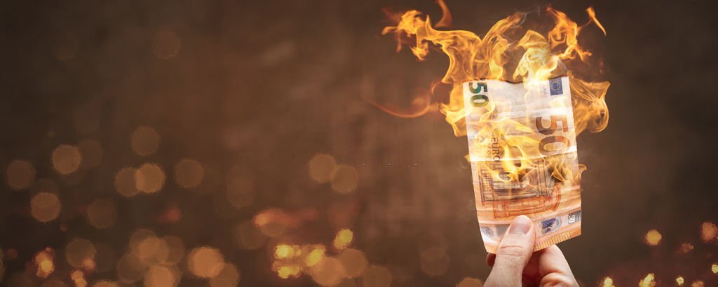 A hand-held 50 Euro banknote is burning with a bright flame. With copy space to the left.