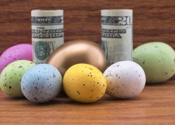 American currency surrounded by gold nest egg and six colored eggs reflect successful diversification in conceptual business investment symbols.